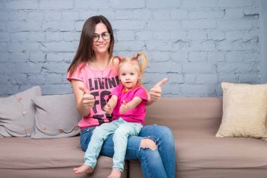 Anne ve bebek oynamak ve eğlenmek kanepede odasında. Onlar parlak giysilerle giyindin. Çekici, şık ve genç ailesi