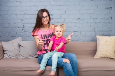 Anne ve bebek oynamak ve eğlenmek kanepede odasında. Onlar parlak giysilerle giyindin. Çekici, şık ve genç ailesi