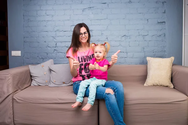 Anne ve bebek oynamak ve eğlenmek kanepede odasında. Onlar parlak giysilerle giyindin. Çekici, şık ve genç ailesi