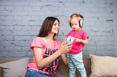 Anne ve kızı büyük kulaklık onların başının üstüne koy kanepede oturan dinleyin. Telefon tutar.