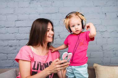 Anne ve kızı büyük kulaklık onların başının üstüne koy kanepede oturan dinleyin. Telefon tutar.