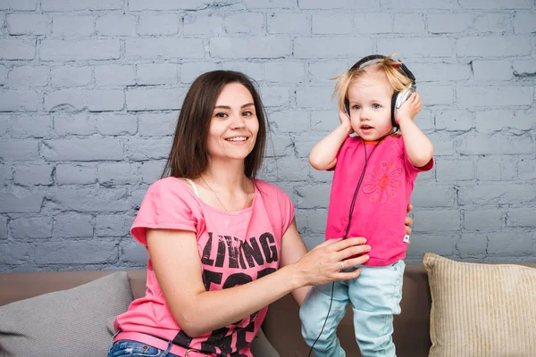 Maman et fille écoutent de la musique dans de gros écouteurs mis sur leur tête, assis sur le canapé. Tient le téléphone . — Photo