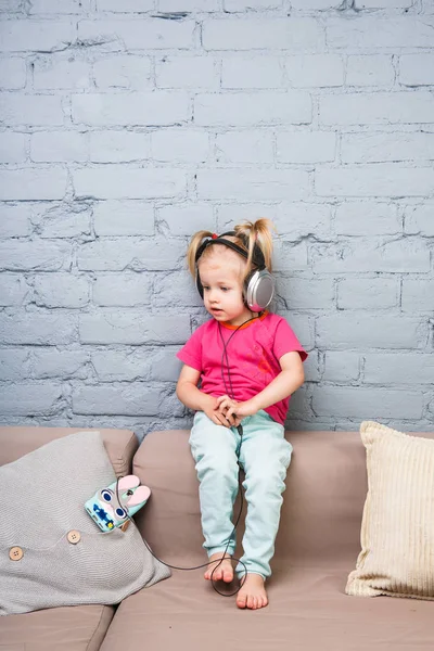 İki yıllık bir küçük kız onun başının üstüne koy kulaklıklar müzik dinlemek koltukta oturuyor. Bir akıllı telefon tutar