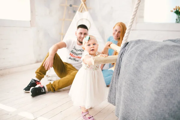 Uma família feliz de três. Mãe, pai, criança de um ano de idade menina em jogo vestido, rir, sorrir no quarto brilhante. Ensolarado — Fotografia de Stock