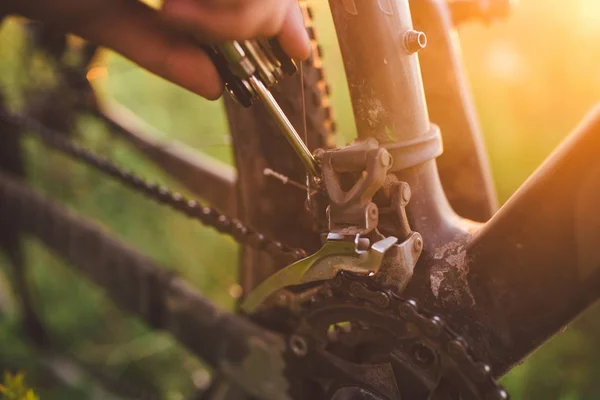 hand with a bicycle tool was engaged in fixing a bicycle outdoors at sunset