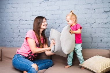 Anne ve kızı kanepe yastık mücadele ile oynamak. Bir odada parlak şık elbise giymiş