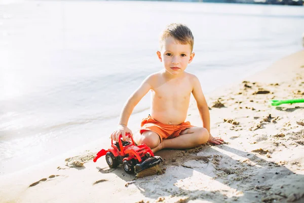 Niño niño jugando en la playa cerca del río juguete rojo tractor —  Fotos de Stock