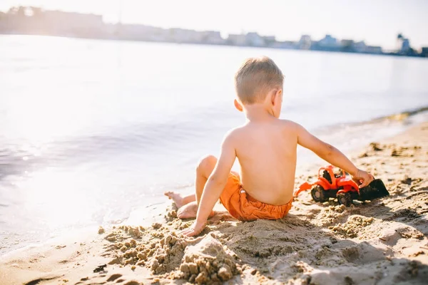 Niño niño jugando en la playa cerca del río juguete rojo tractor —  Fotos de Stock