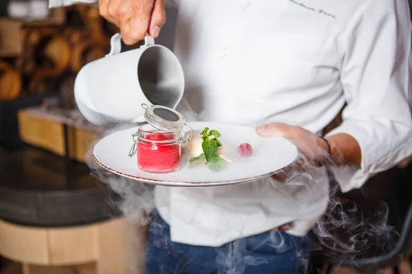Mãos chef segurando um prato branco com sobremesa de sorvete e derramando do jarro com seco — Fotografia de Stock