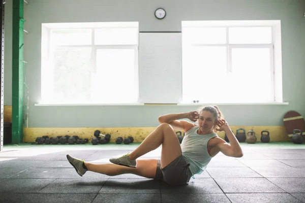 Chica joven y fuerte con una sonrisa haciendo ejercicios para los músculos del estómago, presione en el suelo en la espora — Foto de Stock