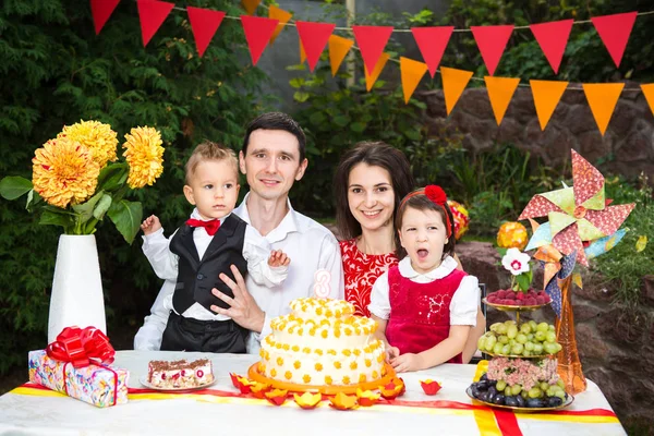 Una famiglia di quattro persone è seduta a un tavolo festivo con una torta e regali. Brutta noiosa vacanza per bambini. Emozione noia, delusione — Foto Stock