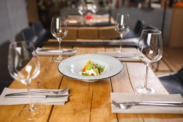 Meja kayu di restoran, disajikan dengan kacamata di tengah, adalah hidangan dengan keju dan sayuran salad vegetarian mozzarella — Stok Foto