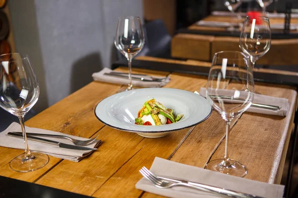 Uma mesa de madeira no restaurante, servida com copos no meio, é um prato com queijo mozzarella salada vegetariana e legumes — Fotografia de Stock