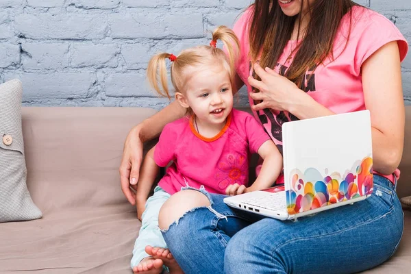 Genç anne ve iki yaşında sarışın kızı ile parlak baskı kapalı kanepede oturan dizüstü bilgisayar laptop beyaz kullanın — Stok fotoğraf