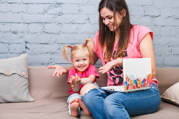 Genç anne ve iki yaşında sarışın kızı ile parlak baskı kapalı kanepede oturan dizüstü bilgisayar laptop beyaz kullanın — Stok fotoğraf