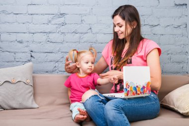 Genç anne ve iki yaşında sarışın kızı ile parlak baskı kapalı kanepede oturan dizüstü bilgisayar laptop beyaz kullanın