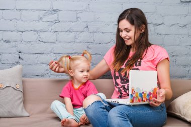 Genç anne ve iki yaşında sarışın kızı ile parlak baskı kapalı kanepede oturan dizüstü bilgisayar laptop beyaz kullanın
