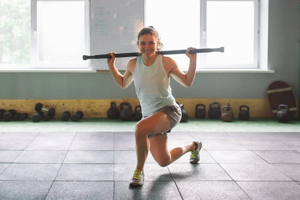 Bela jovem fazendo exercícios de sentar-se com uma vara de peso nas nádegas no ginásio — Fotografia de Stock