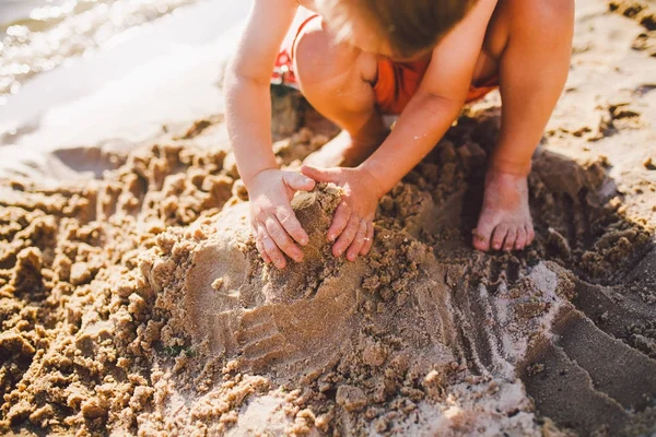 Un niño construye figuras de la arena en la orilla del estanque al atardecer del día, las manos desentierran la arena en plan crujiente —  Fotos de Stock