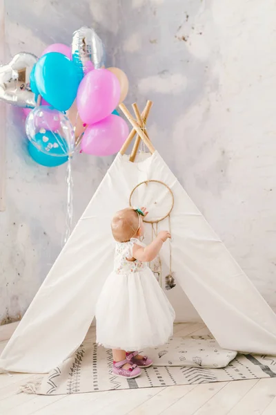 The holiday is the child's birthday one year. A blonde girl in a dress is perpetually inside the interior in light colors and an Indian tipi tent. Inflatable balls with helium colored in t air