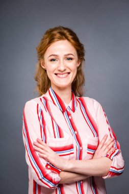 Studio gri izole arka plan üzerinde genç bir kızıl saçlı güzel kız portresi. Bir kadın duruyor ve kısa kollu ile kırmızı gömlekli gülümsüyor. İş kavramı