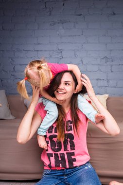 Sarışın kızı onun omuzları üzerinde ince bir genç güzel annesiyle oynamak, zevk ve sofa ahşap zemin üzerinde yakın takım şımartın