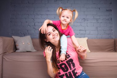 Sarışın kızı onun omuzları üzerinde ince bir genç güzel annesiyle oynamak, zevk ve sofa ahşap zemin üzerinde yakın takım şımartın