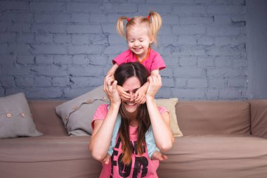 Sarışın kızı onun omuzları üzerinde ince bir genç güzel annesiyle oynamak, zevk ve sofa ahşap zemin üzerinde yakın takım şımartın