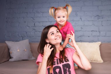 Sarışın kızı onun omuzları üzerinde ince bir genç güzel annesiyle oynamak, zevk ve sofa ahşap zemin üzerinde yakın takım şımartın