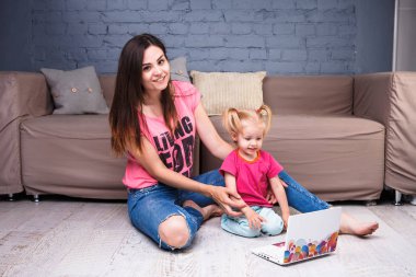 güzel genç şık beyaz anne ile sarışın kızı odanın içinde odasında bir ahşap zemin kanepede oturan bir taşınabilir bilgisayar kullanarak