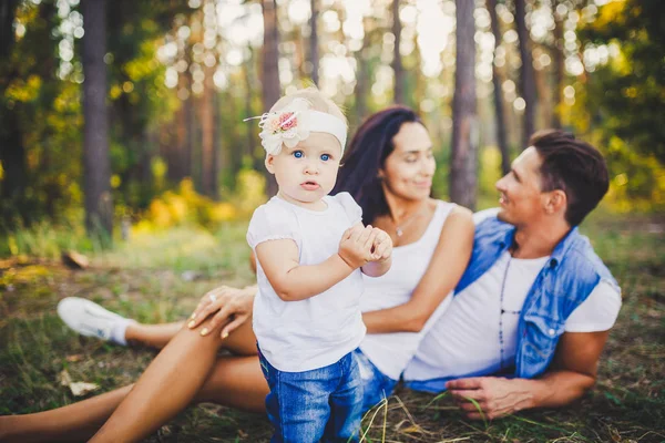 Menina um ano no fundo dos pais descansando na grama aprendendo a andar na natureza no parque. Os primeiros passos de uma criança — Fotografia de Stock