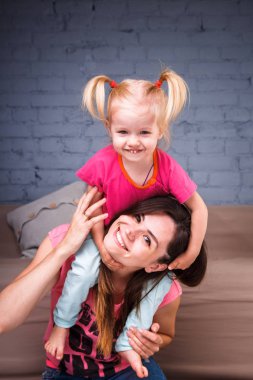 Sarışın kızı onun omuzları üzerinde ince bir genç güzel annesiyle oynamak, zevk ve sofa ahşap zemin üzerinde yakın takım şımartın