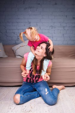 Sarışın kızı onun omuzları üzerinde ince bir genç güzel annesiyle oynamak, zevk ve sofa ahşap zemin üzerinde yakın takım şımartın