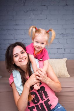 Sarışın kızı onun omuzları üzerinde ince bir genç güzel annesiyle oynamak, zevk ve sofa ahşap zemin üzerinde yakın takım şımartın