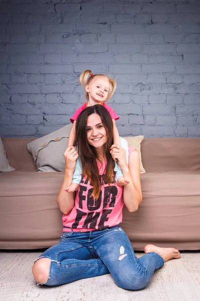 Sarışın kızı onun omuzları üzerinde ince bir genç güzel annesiyle oynamak, zevk ve sofa ahşap zemin üzerinde yakın takım şımartın