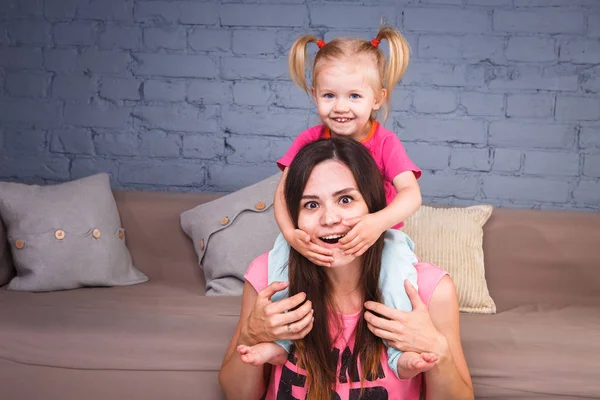 Sarışın kızı onun omuzları üzerinde ince bir genç güzel annesiyle oynamak, zevk ve sofa ahşap zemin üzerinde yakın takım şımartın
