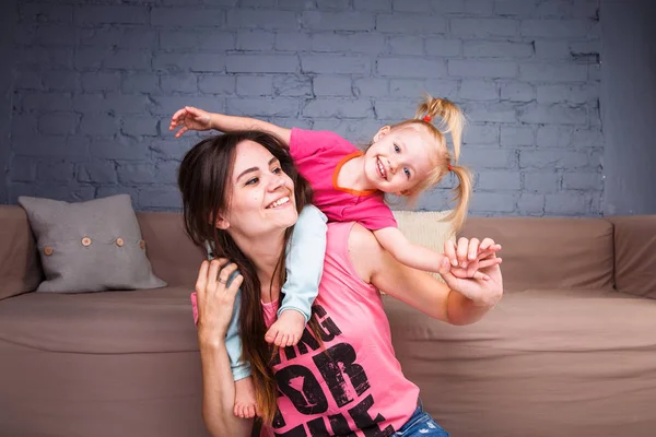 Sarışın kızı onun omuzları üzerinde ince bir genç güzel annesiyle oynamak, zevk ve sofa ahşap zemin üzerinde yakın takım şımartın