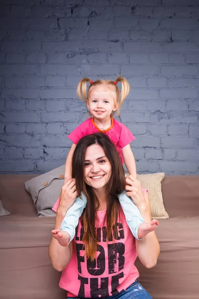 Mladé štíhlé krásná matka s dcerou blond na svých ramenou hrát, užívat a oddávat se týmy u pohovky na dřevěnou podlahu — Stock fotografie