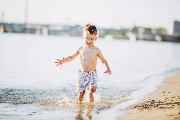Мальчик играет делает всплески, бьет руками по воде в реке на закате — стоковое фото