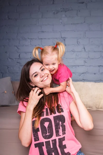 Sarışın kızı onun omuzları üzerinde ince bir genç güzel annesiyle oynamak, zevk ve sofa ahşap zemin üzerinde yakın takım şımartın