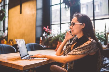 Güzel genç esmer kadının içinde café Noel iç ahşap masa pencerenin telefonda konuşurken ve laptop arıyorum. Kışın, o bir gri örgü kazak ve gözlük giymiş
