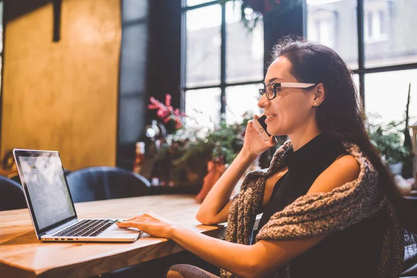 Güzel genç esmer kadının içinde café Noel iç ahşap masa pencerenin telefonda konuşurken ve laptop arıyorum. Kışın, o bir gri örgü kazak ve gözlük giymiş