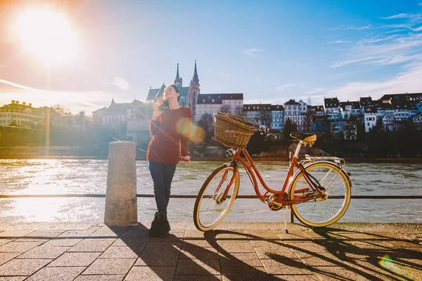 Красива молода дівчина стоїть на набережній біля міста велосипед з кошиком червоного у Швейцарії, місто Базеля. Сонячний день в старій Європі — стокове фото