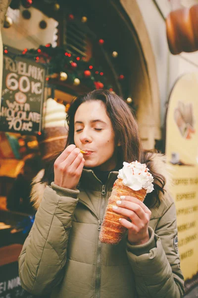 Krásná dívka v teplé bundě jí trdelník nebo Trdlo se smetanou v dlaních, v zimě v České republice, Praha na vánočním trhu — Stock fotografie