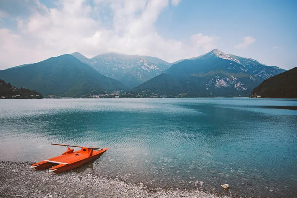 Italia vedere la un lac de munte lago di ledro cu o plajă și o barcă de salvare catamaran de culoare roșie în timpul verii, în vreme tulbure — Fotografie, imagine de stoc
