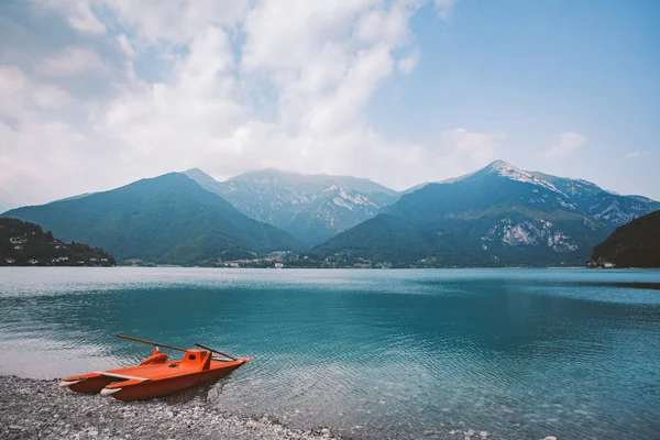 Italia vedere la un lac de munte lago di ledro cu o plajă și o barcă de salvare catamaran de culoare roșie în timpul verii, în vreme tulbure — Fotografie, imagine de stoc