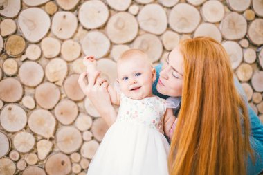 Bir yaşında evde ağaçlar dilim şeklinde ahşap duvar çerçevede bir kızı yürümeyi öğrenme genç redhaired anne. Çocuk beyaz kabarık elbise giymiş. Aile kavramı
