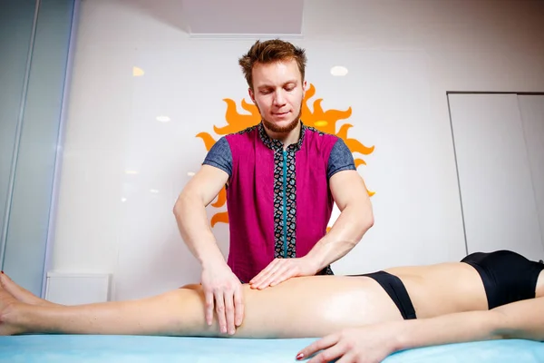 El concepto de masaje y salud. Un masajista masculino hace drenaje linfático y masaje para tonificar los músculos de una chica en ropa interior negra sobre una mesa en una sala fisiológica . — Foto de Stock