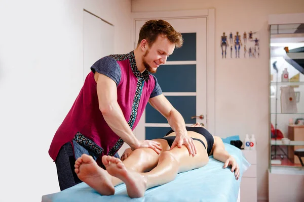 El concepto de masaje y salud. Un masajista masculino hace drenaje linfático y masaje para tonificar los músculos de una chica en ropa interior negra sobre una mesa en una sala fisiológica . —  Fotos de Stock