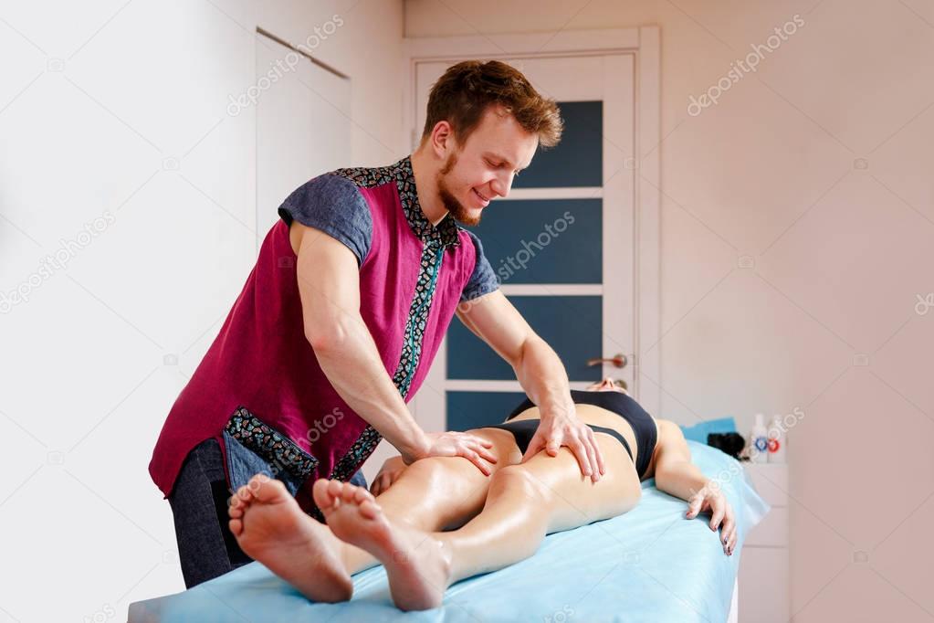 The concept of massage and health. A male massage therapist does lymphatic drainage and massage for toning the muscles of a girl in black underwear on a table in a physiological room.